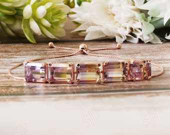 May include: A rose gold adjustable bracelet with a row of five rectangular, multi-colored gemstones. The gemstones are shades of purple, pink, yellow, and green.