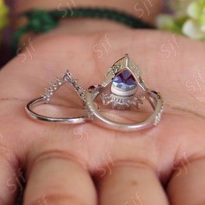 May include: A silver ring set with a pear-shaped blue gemstone surrounded by smaller clear gemstones. The ring is on a hand.