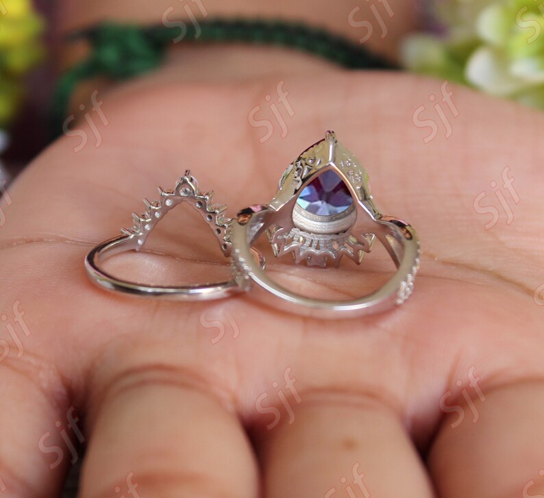 May include: A silver ring set with a pear-shaped blue gemstone surrounded by smaller clear gemstones. The ring is on a hand.