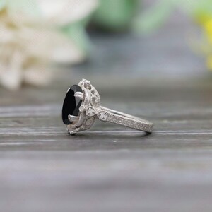 May include: A silver engagement ring with a black oval gemstone and intricate filigree details. The ring is set on a wooden surface.