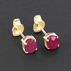 May include: A pair of gold stud earrings with round, red ruby gemstones.