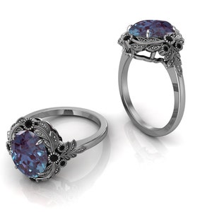 Puede incluir: Dos anillos de plata con un dise&ntilde;o floral ornamentado. Cada anillo presenta una gran piedra preciosa ovalada de color azul-p&uacute;rpura, rodeada de piedras negras m&aacute;s peque&ntilde;as y hojas de plata detalladas. Los anillos se muestran sobre un fondo blanco.