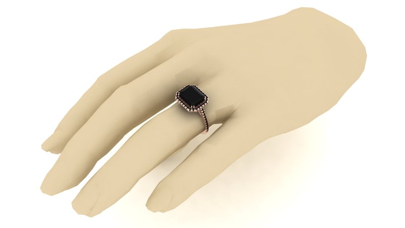 Op de afbeelding: Een ros&eacute;gouden ring met een grote, rechthoekige zwarte edelsteen. De edelsteen is omgeven door een halo van kleinere stenen. De ring wordt op een hand getoond.