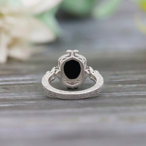 May include: A silver ring with an oval black gemstone set in a filigree design. The band is also decorated with intricate filigree.