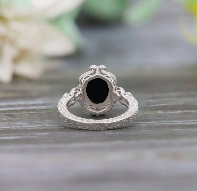 May include: A silver ring with an oval black gemstone set in a filigree design. The band is also decorated with intricate filigree.