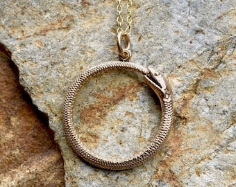 May include: A gold snake pendant necklace with a snake forming a circle. The snake's head is visible at the top of the circle.