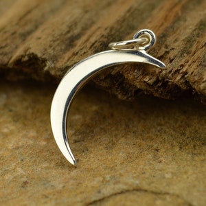 May include: A polished silver crescent moon pendant. The moon shape is smooth and curved, with a small loop at the top for a chain. The pendant is set against a natural, textured background.