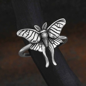 May include: A silver ring featuring a detailed, three-dimensional design of a luna moth with intricate wing patterns.