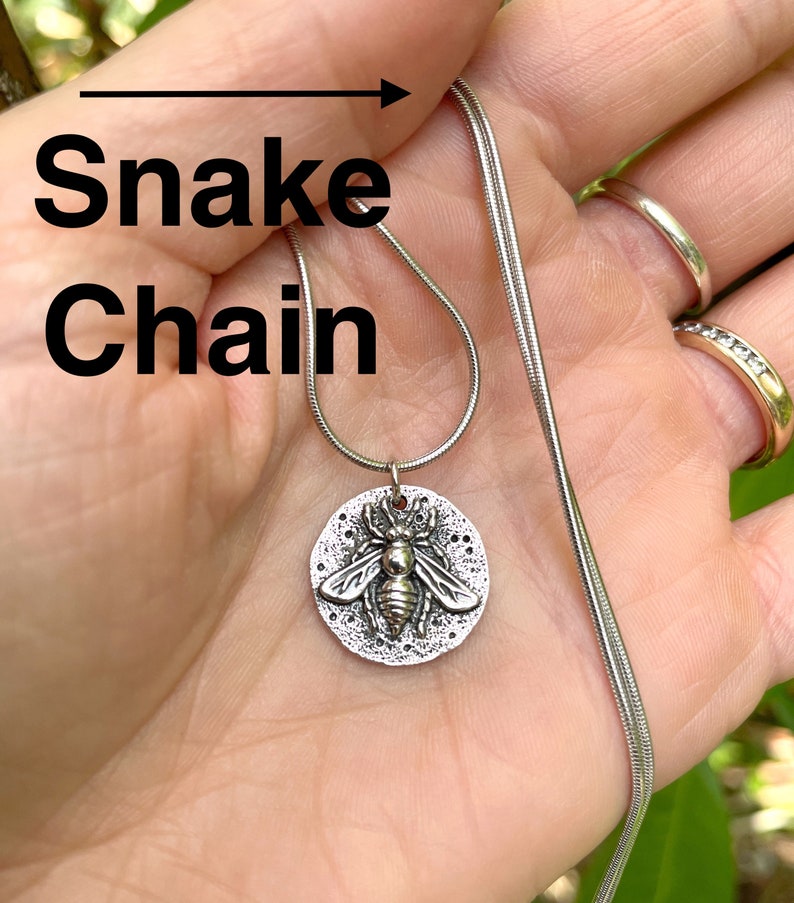 May include: A silver snake chain necklace with a round pendant featuring a detailed bee design.