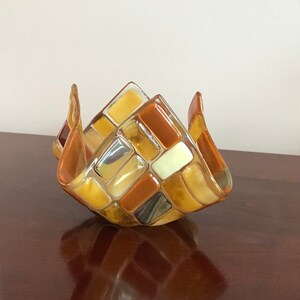 May include: A glass candle holder with a geometric design. The holder is made of clear glass with brown, yellow, and white squares.