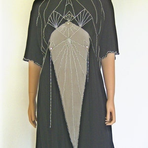 Pode incluir: Um vestido preto com um design geom&eacute;trico e um painel de tecido cinza na frente. O vestido tem um decote alto e mangas curtas.