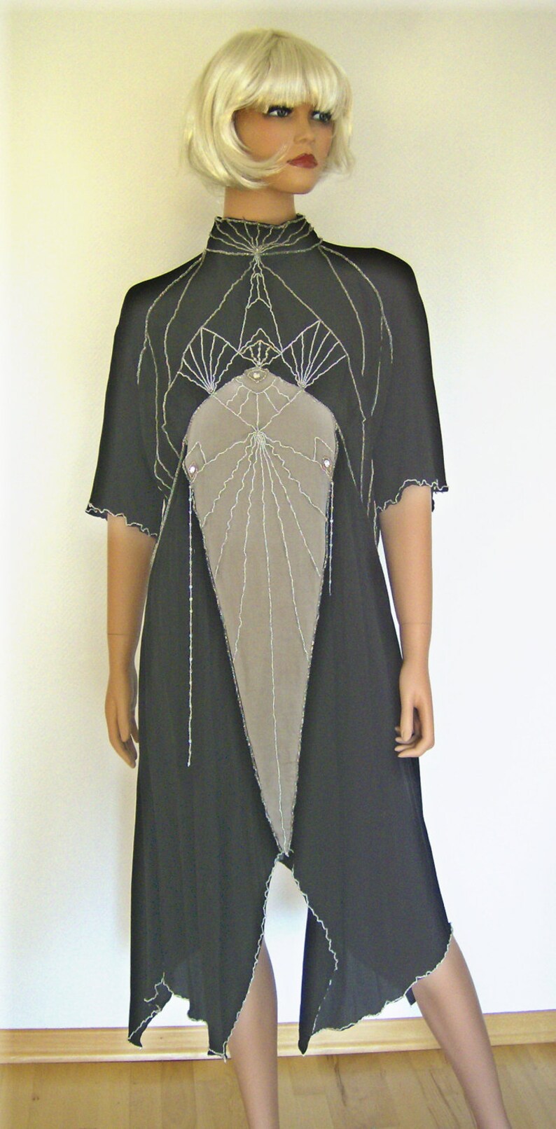 Pode incluir: Um vestido preto com um design geom&eacute;trico e um painel de tecido cinza na frente. O vestido tem um decote alto e mangas curtas.