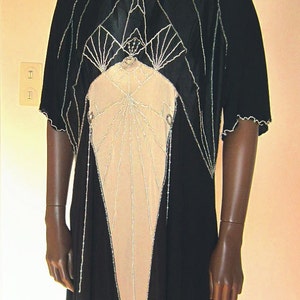 Pode incluir: Um vestido preto e bege com contas com um design geom&eacute;trico. O vestido tem um decote alto e mangas curtas. O vestido &eacute; feito de um tecido transparente e tem uma borda de contas.