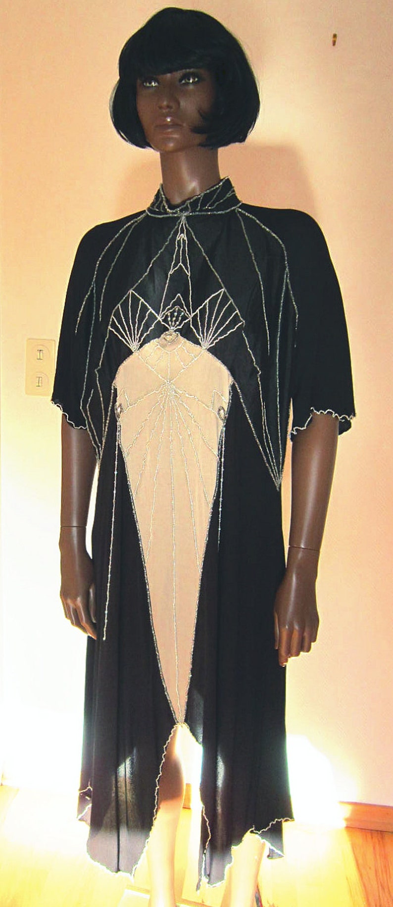 Pode incluir: Um vestido preto e bege com contas com um design geom&eacute;trico. O vestido tem um decote alto e mangas curtas. O vestido &eacute; feito de um tecido transparente e tem uma borda de contas.