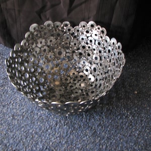 May include: A silver bowl made from a collection of metal washers. The bowl is round and has a slightly flared lip.
