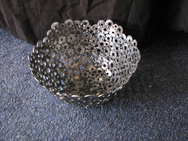 May include: A silver bowl made from a collection of metal washers. The bowl is round and has a slightly flared lip.