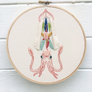 May include: Embroidered squid with pink tentacles and a colorful, patterned head in a wooden embroidery hoop.