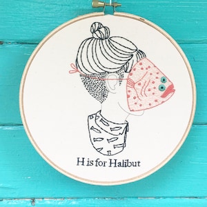 May include: Embroidered hoop art featuring a person with a halibut fish mask. The text "H is for Halibut" is below the image.