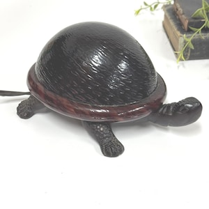 May include: A dark brown turtle-shaped decorative box with a glossy, textured shell that functions as a lid. The base of the box features a smooth, dark reddish-brown rim, while the head, legs, and tail are carved with detailed scale patterns.