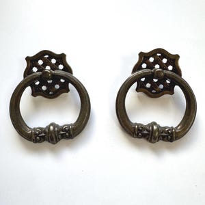 May include: Two antique-style bronze cabinet door pulls with a ring handle and a decorative lattice design.