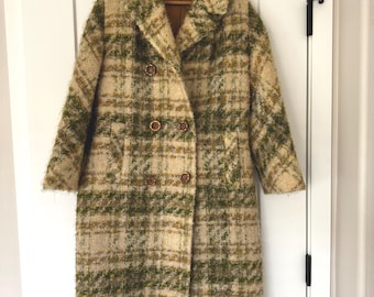 May include: A vintage double-breasted coat in a plaid pattern of green, tan, and cream. The coat has a wide collar, two rows of brown buttons, and long sleeves. It hangs on a wooden hanger against a white door.