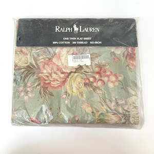 May include: A Ralph Lauren twin flat sheet in a plastic package. The sheet features a floral pattern with pink, yellow, and red flowers on a light green background. The packaging includes the brand name, product details, and material information.