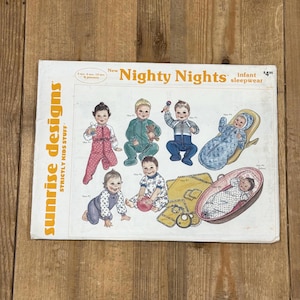 May include: A white paper sewing pattern envelope titled New Nighty Nights infant sleepwear by Sunrise Designs. The front features illustrations of infants wearing various sleepwear styles, including footed pajamas, a bunting, and a swaddle.
