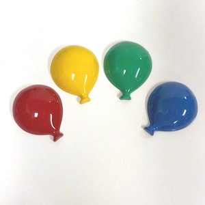 May include: Four balloon-shaped wall hooks or decorative ornaments in solid, glossy colors. The set includes one red, one yellow, one green, and one blue piece, each featuring a smooth, rounded top and a small, tapered knot at the bottom.