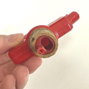 Puede incluir: Un tap&oacute;n de botella de pl&aacute;stico rojo con un inserto de corcho. El tap&oacute;n tiene forma cil&iacute;ndrica con un asa en un extremo. El corcho es de color marr&oacute;n claro y encaja en la abertura de la botella. El tap&oacute;n est&aacute; dise&ntilde;ado para sellar una botella.
