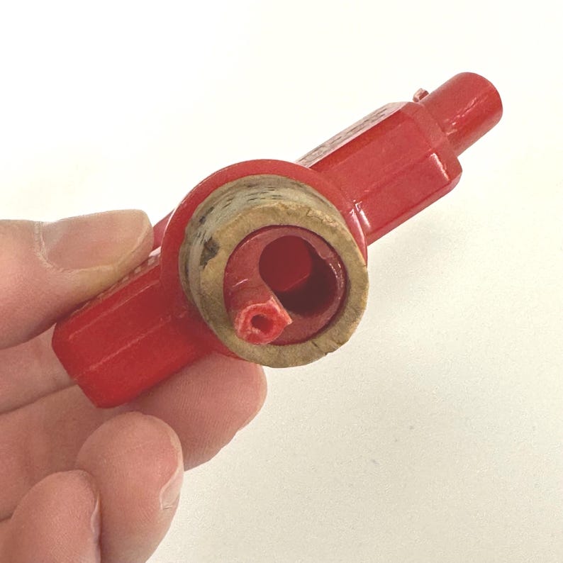 Puede incluir: Un tap&oacute;n de botella de pl&aacute;stico rojo con un inserto de corcho. El tap&oacute;n tiene forma cil&iacute;ndrica con un asa en un extremo. El corcho es de color marr&oacute;n claro y encaja en la abertura de la botella. El tap&oacute;n est&aacute; dise&ntilde;ado para sellar una botella.