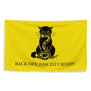 May include: A yellow flag featuring a black silhouette of a cat consuming a snake. The text "BACK OFF, FASCIST CREEPS" is printed beneath the image.
