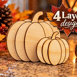 May include: Two light-coloured wooden pumpkin cutouts featuring a 4 Layer design. The larger pumpkin is positioned behind a smaller pumpkin, both displaying smooth, natural wood grain surfaces with dark, laser-cut edges and distinct vertical segments.