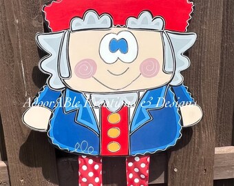 May include: A wooden Uncle Sam door hanger with a red, white, and blue hat, blue jacket, red pants with white polka dots, and blue shoes. The hanger is decorated with a white star on the hat and a blue bow tie.