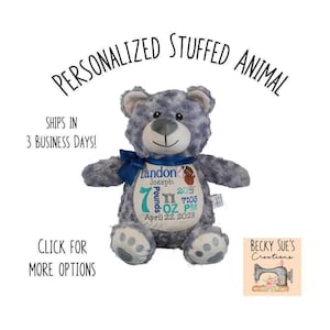 May include: A gray plush teddy bear with a dark blue ribbon around its neck. The bear features an embroidered white patch on its chest displaying the name Landon Joesph, a basketball graphic, and birth details including 7 pounds 11 ounces.