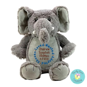 May include: A plush gray elephant stuffed animal with large ears and white tusks. The belly features blue embroidered text reading Chosen, Loved, Wanted, Adopted, surrounding the brown embroidered name Andrew Stephen Holmes and date 4-7-2020.
