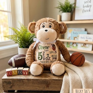 May include: A plush brown monkey toy with a white ribbon around its neck. The monkey's belly features embroidered text: Oliver Lee, 5 Pounds 7 Ounces, 19 1/2 inches, 8:18 PM, June 20, 2025, and graphics of a football and a basketball.