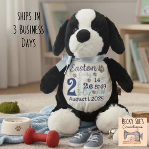 May include: A plush black and white dog toy with a light blue ribbon around its neck. The white chest area features embroidered text including the name Easton, birth date August 1, 2025, and birth details: 2 pounds, 2.6 ounces, and 8:49 AM.