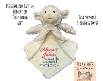 May include: A cream-colored plush lamb security blanket featuring soft, fuzzy fur and a smooth fabric center. Embroidered in pink and grey thread is the name Abigail James, the word Baptized, the date 2/2/2025, and a small cross icon.