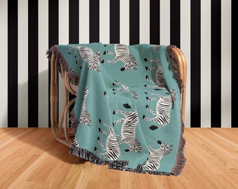 Könnte beinhalten: Eine tealfarbene gewebte Wolldecke mit einem schwarz-weißen Zebra-Muster. Die Decke liegt über einem Korbstuhl vor einer schwarz-weiß gestreiften Wand.