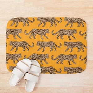 May include: A yellow bath mat with a repeating pattern of brown and black leopard print. The leopard print is a stylized design of a walking leopard.