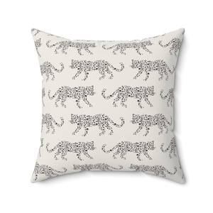 May include: Square throw pillow with a repeating pattern of black leopard silhouettes on a cream background. The pillow has a soft, textured appearance and is designed for decorative use on sofas or beds.