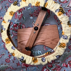 May include: A yellow fabric chair cushion with a bee pattern. The cushion is round and has a drawstring closure. The cushion is on top of a wooden chair.