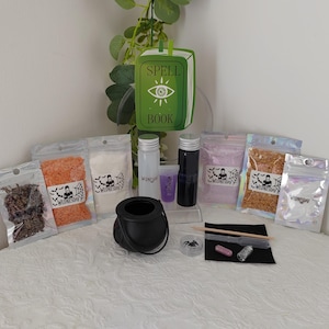 Può includere: Un kit a tema stregoneria con un calderone nero, piccole bottiglie e vari ingredienti in sacchetti trasparenti. Un cartello verde "Spell Book" è sullo sfondo. Le borse hanno un'etichetta "Wednesday".