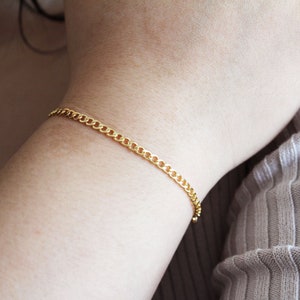May include: A gold chain bracelet with a delicate curb chain design.