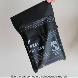 May include: A black compostable mailer bag with the text "I'm a real dirt bag" and "Home Compostable AS 5810 AS/NZS 4738:2003". The bag is designed to be reused and has a cut line with the text "Please cut here so that you can re-use me - Re-use ideas @betterpackagingco".
