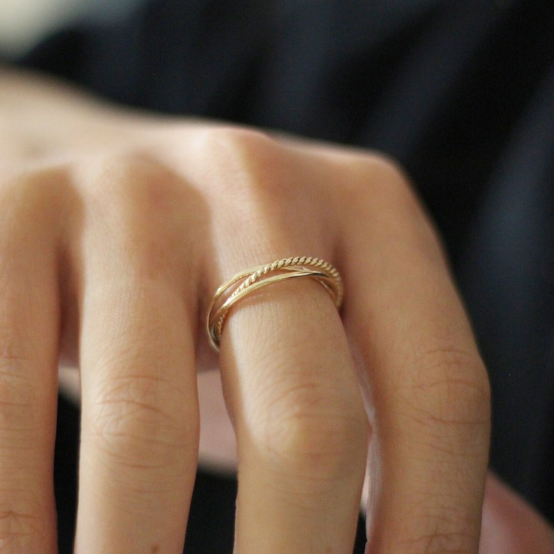 May include: A gold ring with a twisted design. The ring is worn on a finger.