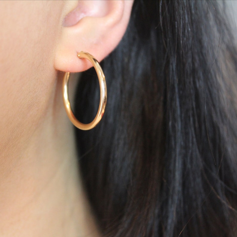 May include: Gold hoop earrings worn in a person's earlobe.