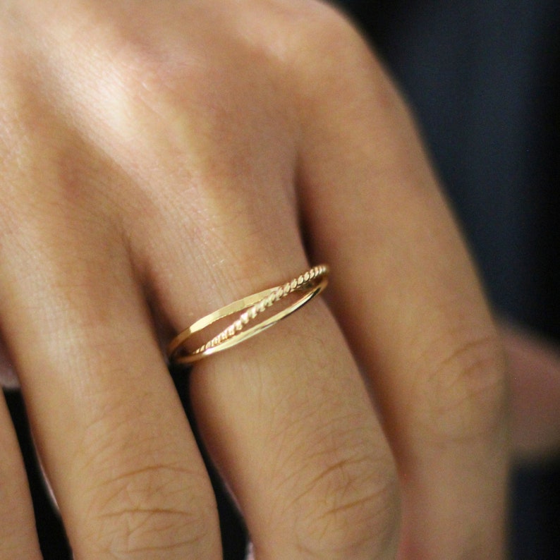 May include: A gold ring with a twisted design. The ring is worn on a finger.
