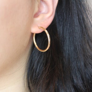 May include: A pair of gold hoop earrings worn in a person's ear.