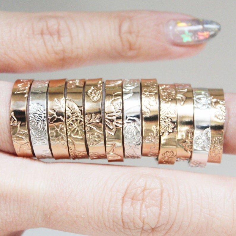 Puede incluir: Una colecci&oacute;n de anillos con dise&ntilde;os florales en tonos dorados y plateados. Los anillos se muestran en un dedo, mostrando los intrincados dise&ntilde;os bot&aacute;nicos. Los anillos parecen ser de metal y presentan varios patrones florales y de hojas.